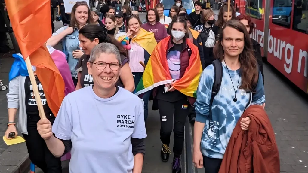 Teilnehmer*innen des Dyke March Würzburg laufen mit Regenbogenflaggen durch die Innenstadt, organisiert vom WuF-Zentrum.
